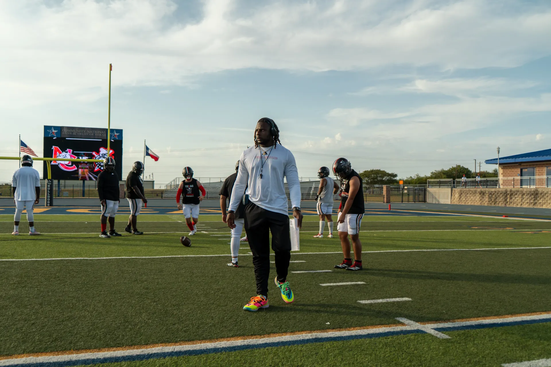 Coach Darnell Newman walking across the football field with players around him