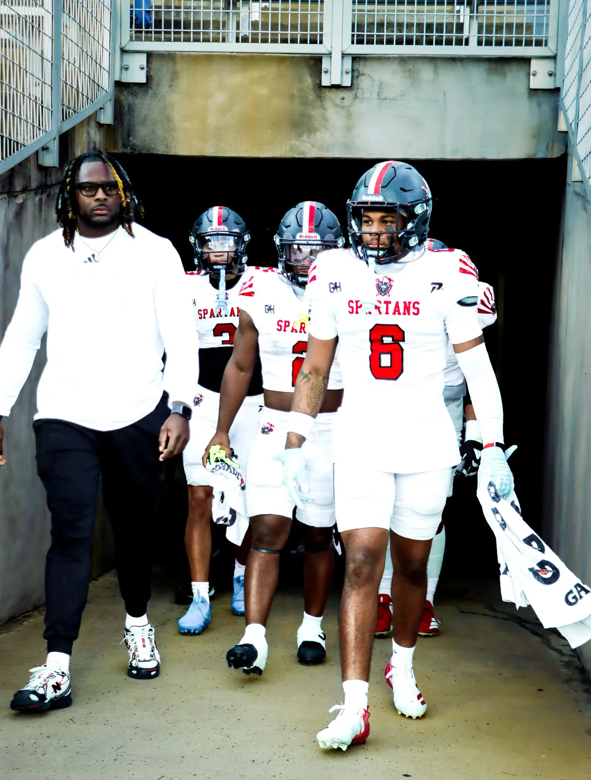 Coach Darnell Newman walking with Texas Spartans players through a stadium tunnel