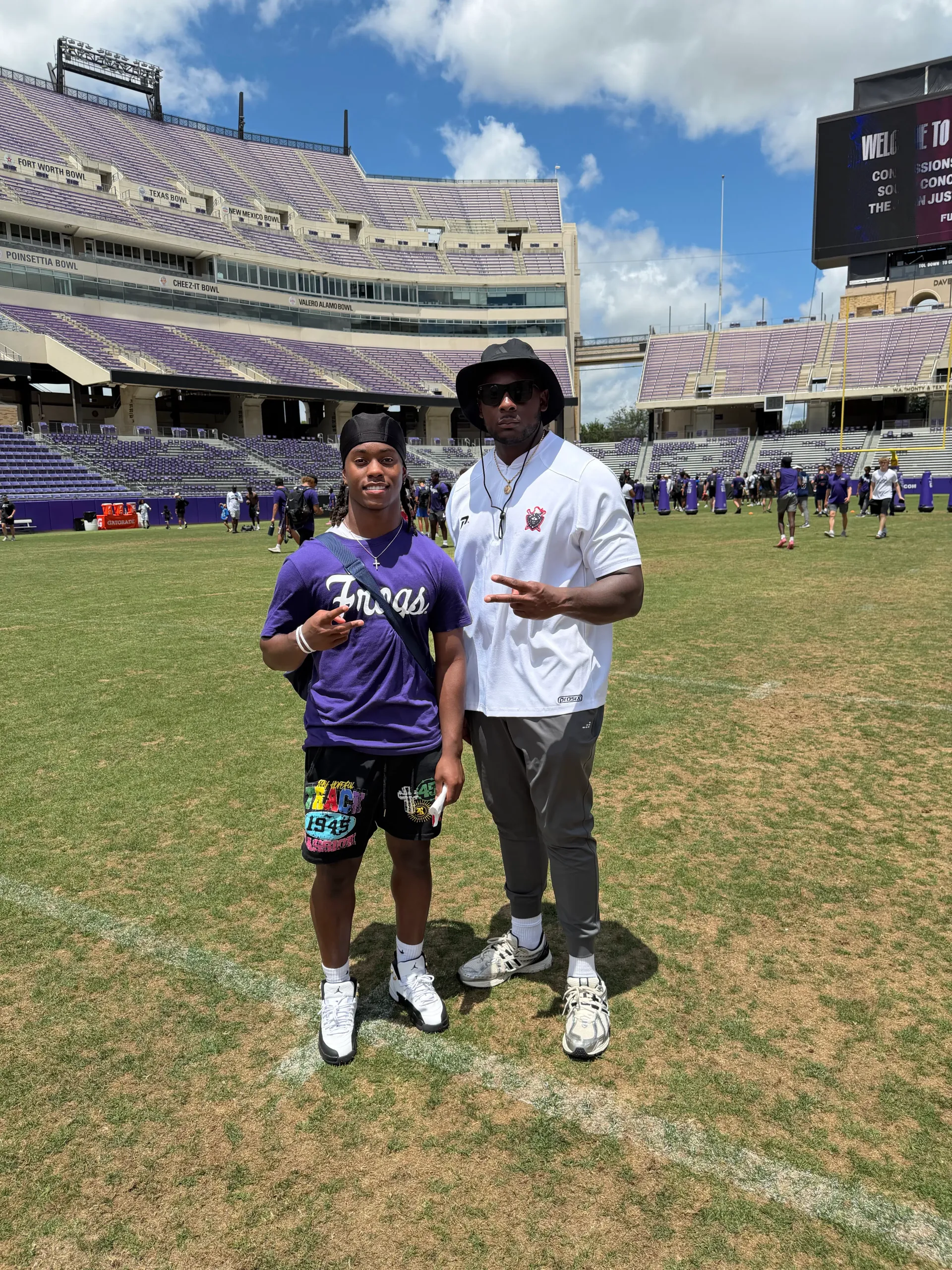 Coach Darnell Newman wearing a bucket hat with a recruit in a Texas shirt on a college stadium field